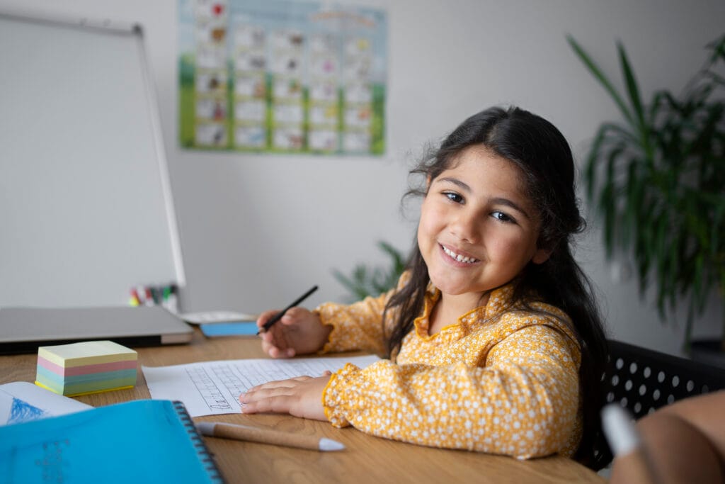 Smiling girl practicing handwriting and spelling during Holistic Spell Bee preparation in Mumbai.