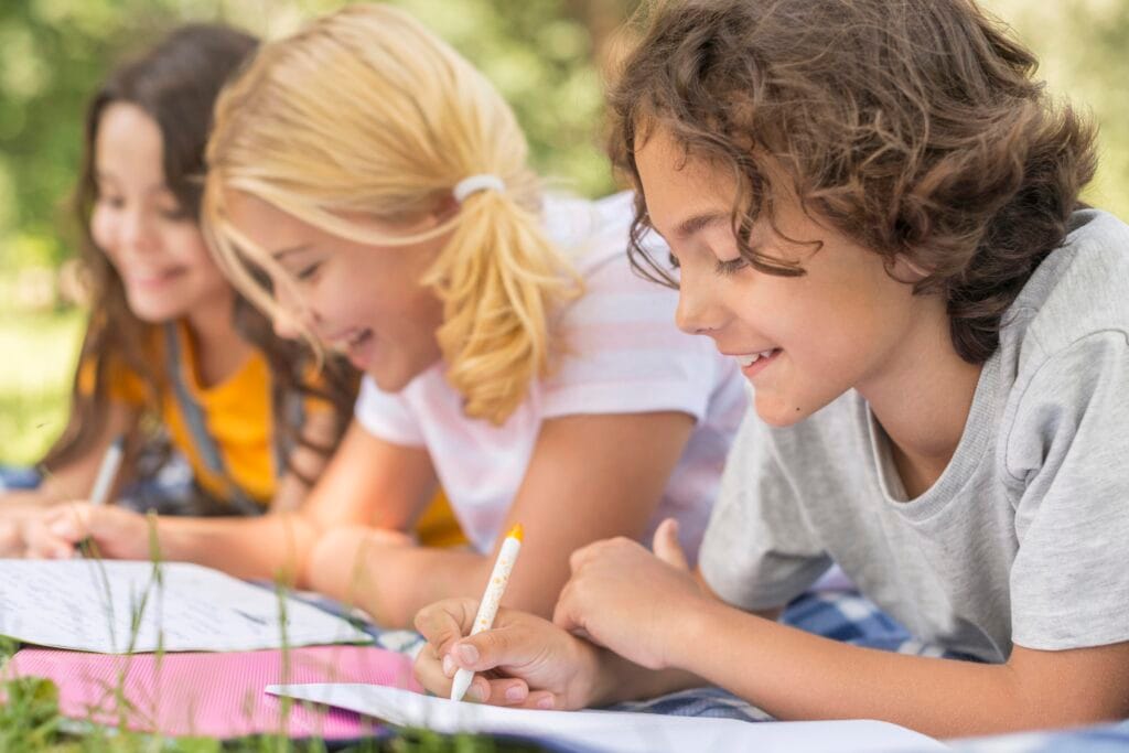 Children happily writing outdoors while preparing for ADA Holistic Spell Bee competitions in Bahrain.