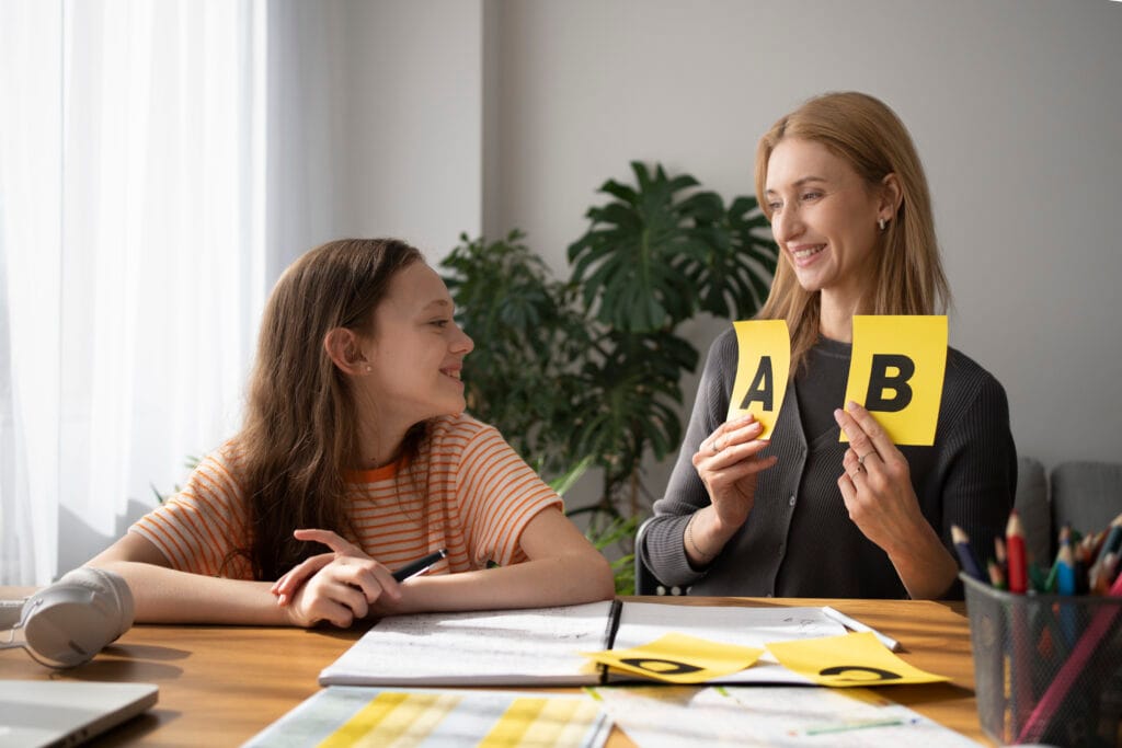 A teacher teaching phonics with alphabet flashcards to a smiling young girl during a holistic phonics session in Bangalore.