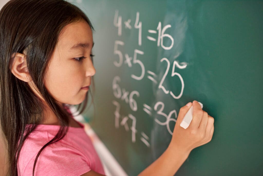 Girl solving multiplication problems on chalkboard – Why parents prefer ADA Holistic Vedic Maths for kids.