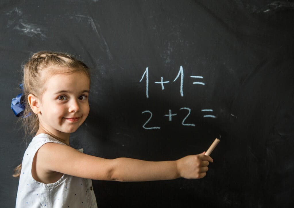 Smiling young girl solving basic math equations on a blackboard with 10X Confidence at Achievers Destination Academy’s Vedic Maths classes in Aurangabad.