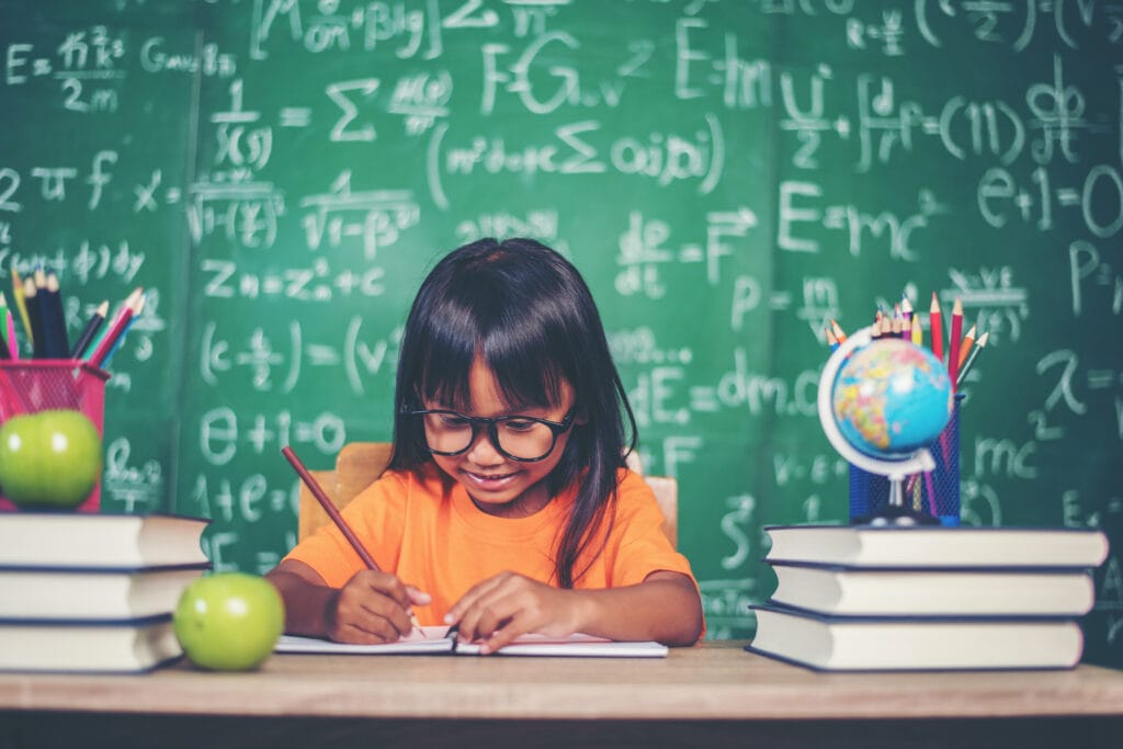 Smiling girl studying with books and chalkboard full of equations – real-life applications of Vedic Maths.