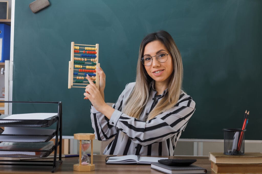 Confident young woman teacher holding an abacus in a classroom, symbolizing women empowerment through education and online abacus training.